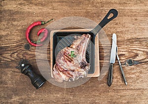 Cooked meat rib eye steak with spices, red chili, rosemary and vintage silverware incookinf pan over rustic wooden