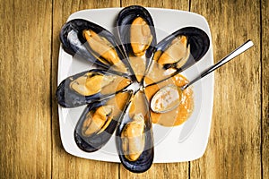 Cooked mussels with parsley and orange sauce and half a lemon on a white plate