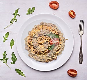 Cooked pasta with turkey and onions, tomatoes arugula on a white plate with a fork on wooden rustic background top view