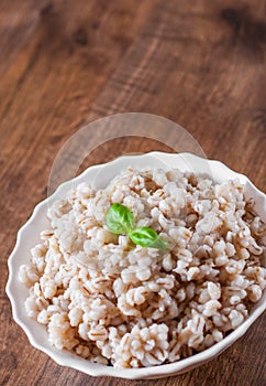 Cooked pearl barley in bowl on a wooden table