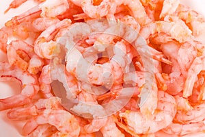 Cooked and peeled shrimp tails on white dish close-up