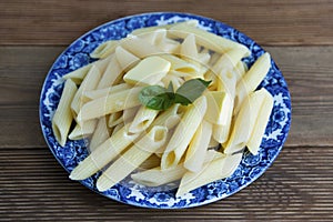 Cooked penne pasta with butter and cheese and basil in vintage beautiful blue plate on wooden table. Isolated. photo