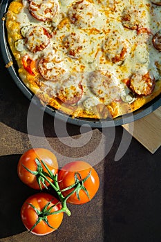 Cooked pizza with fresh tomatoes and sausage top view, close-up, on a dark background, vertical photo