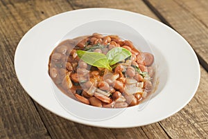 Cooked Red Beans in Tomato Sauce with Spinach and Onion, white Round Plate, Wooden Background, Top view.