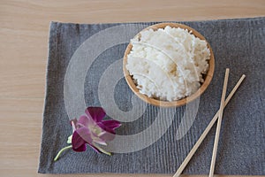 Cooked rice in a wooden bowl and chopsticks on a wood background.