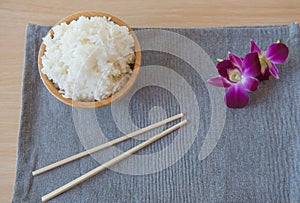 Cooked rice in a wooden bowl and chopsticks on a wood background.