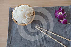 Cooked rice in a wooden bowl and chopsticks on a wood background.