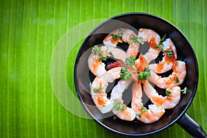 Cooked seafood plate shrimps prawns decorate pan with sauce herbs and spices banana leaf background