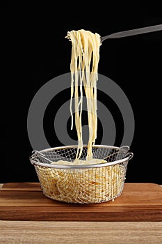 Cooked spaghetti in fork and metal colander on cuttingboard