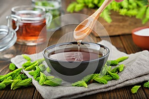 Cooked syrup or honey from spruce tips in a black bowl, jar of jam or honey from fir buds and needles.