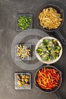 Cooked vegetables on black plate and dark background, baked onion, broccoli, garlic, red and yellow pepper, mushrooms.