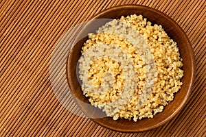 Cooked white quinoa in a dark wood bowl isolated on bamboo matt from above