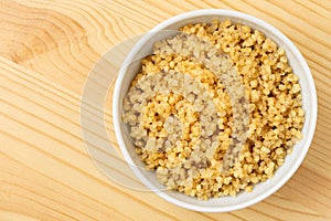 Cooked white quinoa in a white ceramic bowl isolated on light wood from above