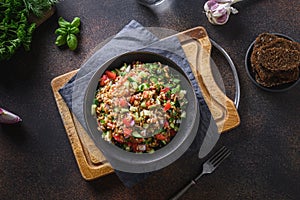 Cooked Whole Grain cereal spelt salad with seasonal vegetables in bowl on brown background.