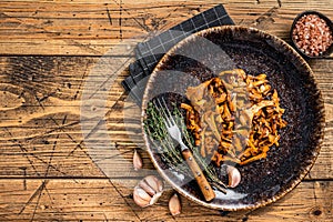 Cooked wild fried chanterelle mushrooms with onions and herbs. Wooden background. Top view. Copy space