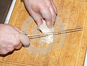 Cooker's hands grind cocoa butter with a knife on a wooden kitchen board to make chocolate