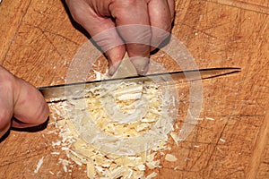 Cooker's hands grind cocoa butter with a knife on a wooden kitchen board to make chocolate