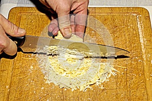 Cooker's hands grind cocoa butter with a knife on a wooden kitchen board to make chocolate