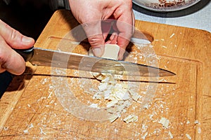 Cooker's hands grind cocoa butter with a knife on a wooden kitchen board to make chocolate