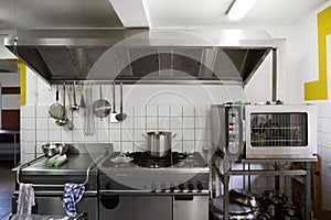 Cooker system from steel with stove, grill, oven and extractor hood in a professional canteen kitchen