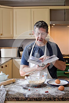 cookery lessons in the kitchen. Man reading a cookery book, Wearing an apron