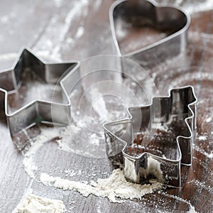 Cookie cutters in the shape of `heart`, `star` and `christmas tree` lie on the table. Focus is on the `Christmas tree` shaped coo