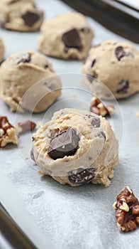 Cookie dough balls with chocolate chunks and walnut pieces arranged on a baking sheet photo