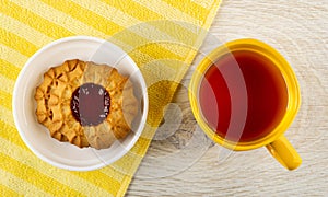 Cookie with jam in saucer on napkin, glass cup with tea on table. Top view