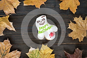 Cookie like a Ghost with the words Happy Halloween on wooden background with autumn leaves