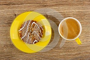 Cookie with sunflower seeds and sesame in yellow saucer, black coffee in cup on table. Top view