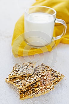 Cookies with cereals and a cup of milk on a white wooden table.