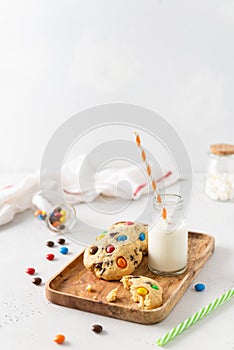 Cookies with colorful candies and chocolate chips and a bottle of milk on white background. Side view, copy space. Multicolor