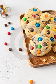 Cookies with colorful candies and chocolate chips on wooden tray on white background. Side view, close up. Multicolor biscuits for