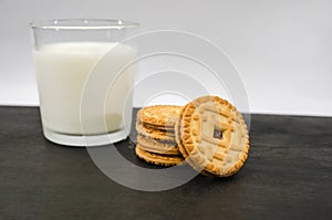 Cookies and a glass of milk on a dark wooden table.