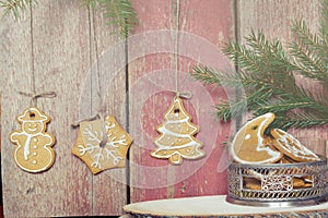 Cookies hang on ropes from a wooden wall, near a vase with Christmas cookies