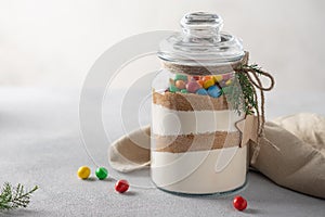 Cookies mix with color candies in jar. glass jar is layered with dry ingredients.