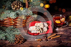 Cookies with poppy seeds, a cup of tea and a basket full of spruce on the wooden natural table. Christmas and New Year lights and