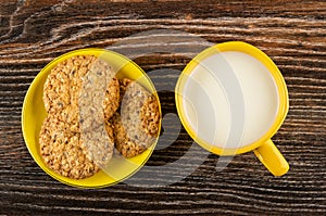 Cookies with sesame and flaxseeds in saucer, cup with milk on wooden table. Top view