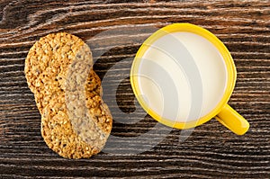 Cookies with sesame and flaxseeds, yellow cup with milk on wooden table. Top view