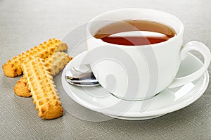 Cookies in shape sticks, cup of tea, spoon on saucer on wooden table
