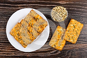 Cookies with sunflower seeds in plate, peeled seeds in bowl on dark wooden table. Top view