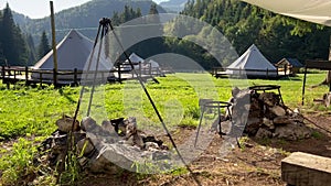 Cooking area with fireplace in glamping tent camp site in green meadow surrounded by fir tree forest