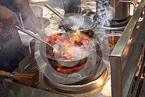 Cooking Asian food from meat and vegetables in a flaming wok outside.
