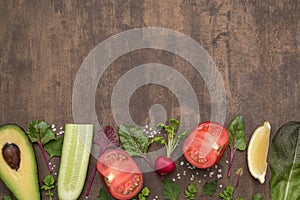 Cooking background with fresh vegetables and herbs. Ingredients for salad on brown table, top view, copy space, flat lay