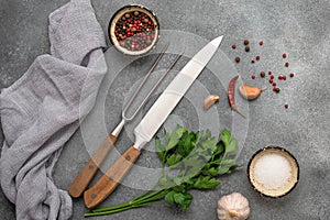 Cooking background, knife, meat fork, spices and greens. Gray concrete background. Top view, flat lay