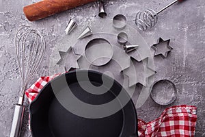 Cooking or baking food background with kitchen utensils, rolling pin, frying pan, cookie cutout on grey wooden background