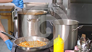 Cooking in canteen. close-up. there are large pots on stove. onions and carrots are fried in pan. the cook, in