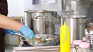 Cooking in canteen. close-up. there are large pots on stove. onions and carrots are fried in pan. the cook, in