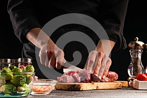 Cooking, the chef cuts pork meat on a background of vegetables. Cooking. Recipe book, cooking and gastronomy