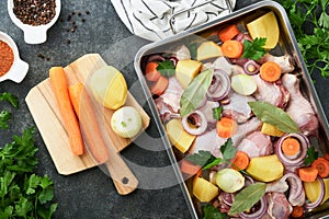 Cooking chicken bouillon or roast in cooking pan or pot with vegetables potatoes, carrots and herbs on kitchen grey concrete